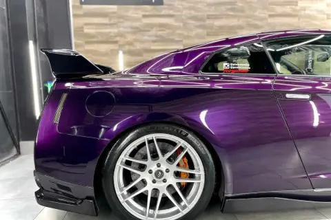 Sportowy Nissan GT-R w odcieniu **midnight purple**, z karbonowym spoilerem i felgami.