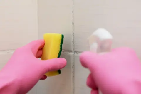 Main rose gantée tient une éponge jaune pour nettoyer une tache sur carrelage qui ne part pas.