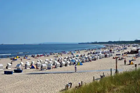 Plaża nad Bałtykiem z rzędami koszy plażowych, ludźmi i morzem w tle.