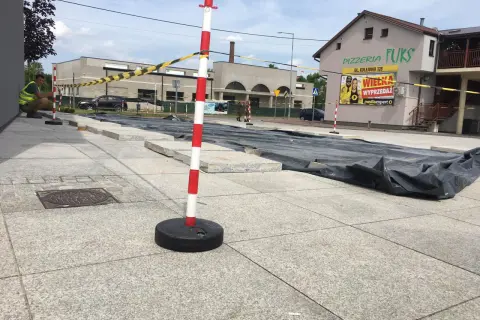 Zabezpieczenie terenu budowy: czerwono-białe słupki i taśma ostrzegawcza oddzielają plac budowy od chodnika.