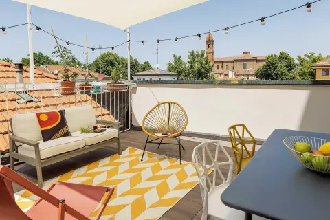 Un accogliente terrazzo sul tetto con divano, sedie colorate e un tappeto geometrico. Ideale per godersi il panorama urbano e rilassarsi.