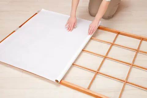 Mains déroulant du papier pour fabriquer une cloison japonaise sur un cadre en bois.