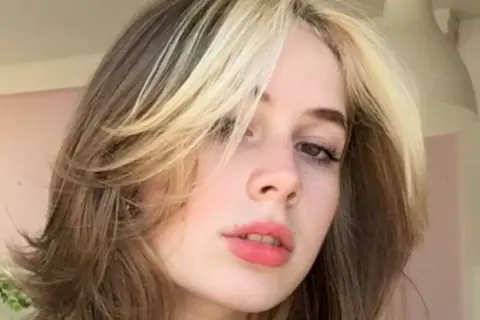 Dziewczyna z modnym wolf cut bez grzywki, z pasemkami blond na ciemniejszych włosach.