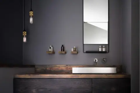 Modernes schwarzes Bad mit Holz. Ein Waschbecken aus Stein auf einem dunklen Holzunterschrank, flankiert von rustikalen Holzregalen mit Pflegeprodukten.