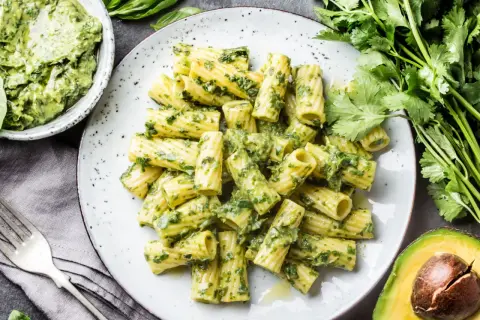 Rigatoni-Nudeln mit cremigem Avocado-Pesto, garniert mit frischem Koriander und Basilikum.