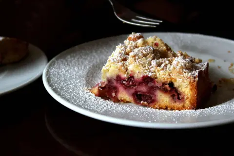 Ein Stück von Omas Kirschkuchen mit Streuseln, bestäubt mit Puderzucker, wartet auf seine Gabel.