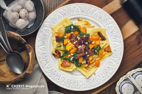 Ravioli mit Kürbis, Spinat und Pinienkernen – ein köstliches ravioli rezept. Daneben Knoblauch und Löffel.