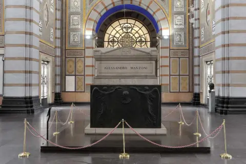 La tomba di Manzoni, imponente monumento con bassorilievi di angeli e ritratto, è protetta da cordoni dorati.