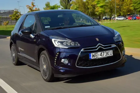 Granatowy Citroen DS3 w ruchu ulicznym. Kierowca w okularach przeciwsłonecznych. Wiele pozytywnych citroen ds3 opinie potwierdza jego styl.