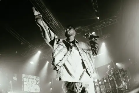 Emis Killa sul palco, con la mano alzata e il microfono in pugno, interpreta i suoi testi, parole di ghiaccio che riscaldano la folla.