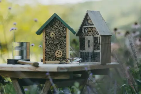Zwei selbstgebaute Insektenhotels stehen auf einem Tisch im Garten. Ein Insektenhotel bauen ist eine tolle Idee für jeden Naturliebhaber.
