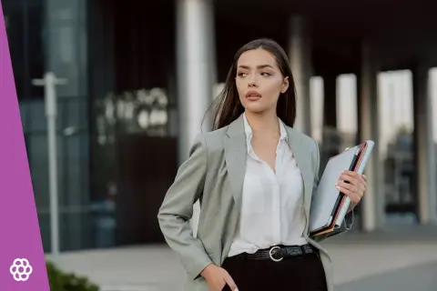 Elegancka kobieta w szarej marynarce i białej koszuli, trzymająca teczkę. Idealny przykład, jak się ubrać do sądu jako świadek – profesjonalnie i z klasą.