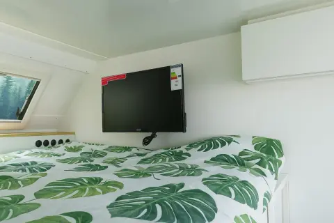 Cama con sábanas de hojas verdes y un televisor de consumo tv 50 pulgadas colgado en la pared.