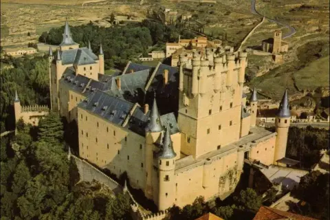 Vista aérea del Alcázar de Segovia, con sus torres y tejados, rodeado de vegetación. La sala de los reyes se intuye en su imponente estructura.