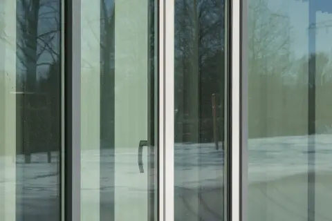 Ventana con cristal planitherm, reflejando árboles y nieve. Un tirador plateado se ve en el panel central.