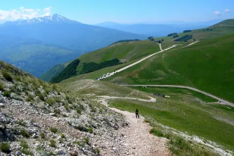 Sentiero roccioso verso la Forca di Presta, con montagne verdi e un cielo azzurro.