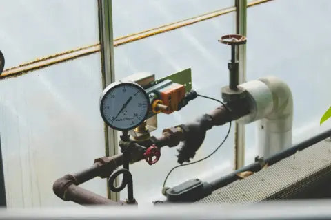 Manometr wskazuje niskie jakie ciśnienie na piecu gazowym. Rury i zawory są częścią instalacji.