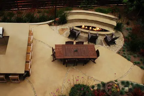 Un elegante giardino con un'area salotto attorno a un focolare, il tutto su un raffinato rivestimento in cemento per esterni.