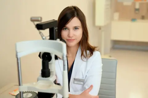 Okulistka przy aparaturze. Jak się przygotować do wizyty u okulisty? Pamiętaj o zabraniu okularów i soczewek.