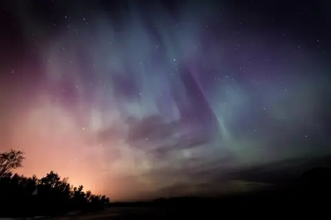 Ciel étoilé aux couleurs de l'aurore boréale, une harmonie du soir qui évoque Baudelaire. Silhouettes d'arbres et de collines dans la nuit.
