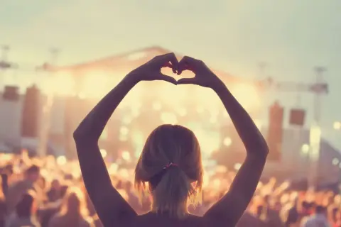 Ragazza fa un cuore con le mani a un concerto, immersa nell'atmosfera delle canzoni romantiche inglesi.