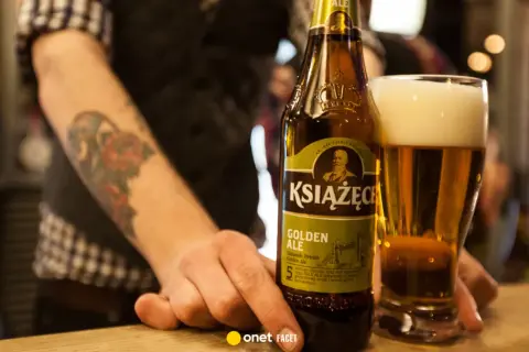 Ręka z tatuażem sięga po butelkę piwa Książęce Golden Ale. Czy to piwo jest gorzkie?