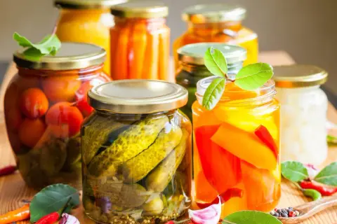 Słoiki z przetworami: ogórki, pomidory, papryka, marchewka. Wskazówka, jak pasteryzować słoiki, by cieszyć się smakami lata przez cały rok.