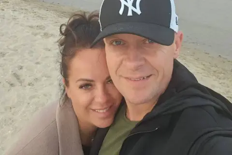 Piotr Marciniak z żoną na plaży, uśmiechnięci i blisko siebie.