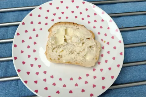 Kromka domowego chleba z masłem na talerzyku w serduszka. Zastanawiasz się, dlaczego domowy chleb się kruszy?