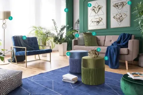 Salon z kanapą, fotelami i pufami. Ściany w kolorze głębokiej zieleni, z obrazami przedstawiającymi diamenty. Wnętrze zdobią rośliny i tekstylia w odcieniach niebieskiego i **kolor szmaragdowy**.