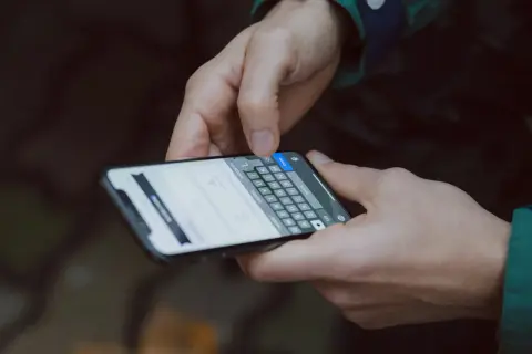 Dłonie trzymają smartfon, na ekranie widać klawiaturę i tekst. To jak instrukcja obsługi telefonu, którą ktoś właśnie czyta.