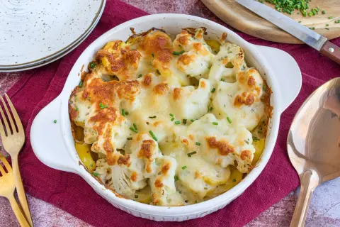 Ein goldbraun überbackener Blumenkohl Kartoffel Auflauf mit geschmolzenem Käse und frischen Kräutern, bereit zum Servieren.