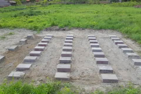 Przygotowana wylewka pod domek narzędziowy. Ułożone bloczki betonowe tworzą fundament na piaszczystym podłożu.