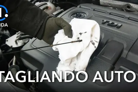 Guida per controllare l'olio motore: si può fare il tagliando da soli. La mano guantata pulisce l'astina dell'olio su un panno bianco.