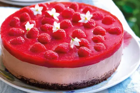 Cheesecake ricetta semplice con lamponi freschi e gelatina rossa, decorata con piccoli fiori bianchi.