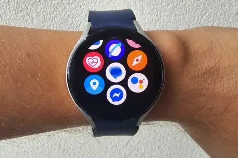 Zegarek z systemem Wear OS na nadgarstku, z widocznymi ikonami aplikacji: serce, lokalizacja, Messenger, Google Assistant i inne.