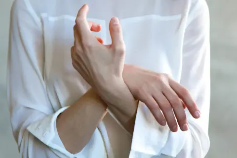 Frau hält ihr Handgelenk, als ob sie einen stechenden Schmerz im Handgelenk bei Drehbewegung spürt.