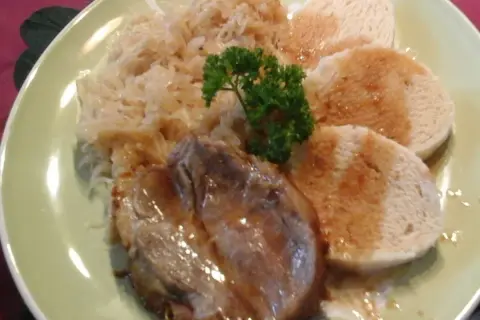 Ein Teller mit tschechischem Schweinebraten, Sauerkraut und Knödeln, garniert mit Petersilie.