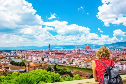 Una donna ammira il panorama di Firenze, la capitale della Toscana, con il Duomo e il Ponte Vecchio sotto un cielo azzurro e nuvoloso.