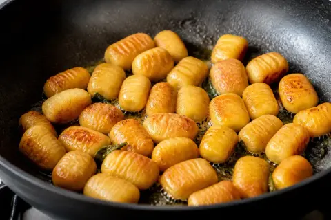Gnocchis dorés et légèrement grillés dans une poêle, prêts pour la cuisson finale.