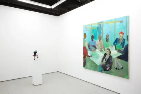 A miniature figure climbs a pedestal in a white-walled gallery, a vibrant painting of a diverse group at a meeting hangs nearby. NYC galleries for emerging artists showcase such intriguing pieces.
