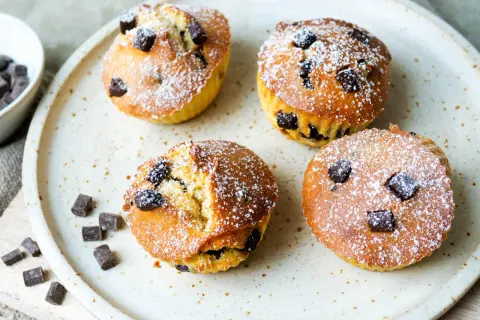 Vier leckere Schoko-Muffins, frisch aus dem Airfryer, mit Puderzucker bestäubt und Schokostückchen.