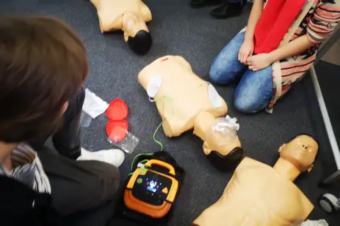 Uczestnicy kpp kursu ćwiczą resuscytację na fantomach. Widać defibrylator i akcesoria do RKO.