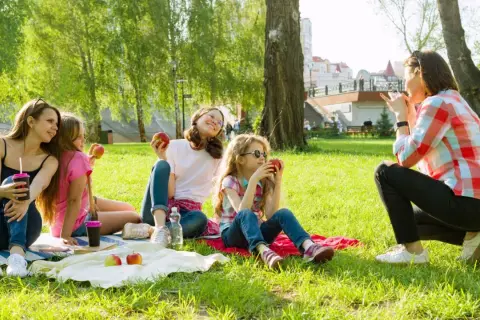 Rodzina na pikniku w parku. Czy Boże Ciało jest dniem wolnym od pracy? Dzieci jedzą jabłka, ciesząc się słońcem.