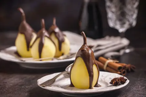 Poires pochées nappées de chocolat, un délice de poire belle Hélène. Cannelle et anis étoilé en arrière-plan.