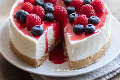 Cheesecake ricetta: torta cremosa con base croccante, guarnita con lamponi, mirtilli e coulis rosso.