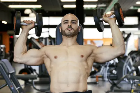 Uomo calvo con barba solleva manubri in palestra, allenamento per il **total body**.