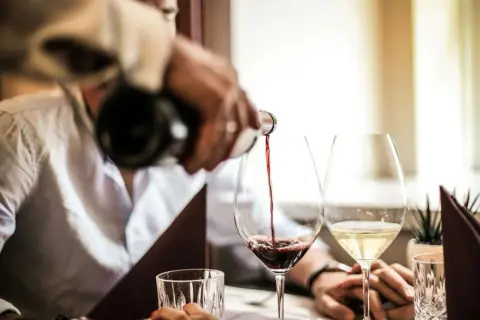 Versando vino rosso in un calice, scoprendo il significato di vino fermo. Accanto, un bicchiere di vino bianco.
