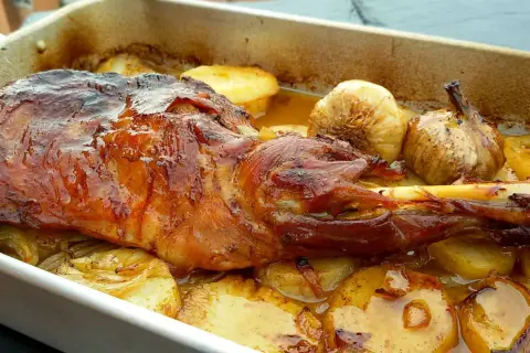 Paletilla de cordero al horno, dorada y jugosa, con patatas y ajos asados. El tiempo y temperatura perfectos para un plato delicioso.