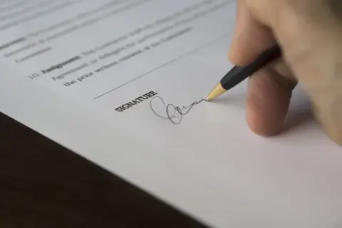 Dłoń z długopisem składa podpis na dokumencie. To jest parafka, co to znaczy? To potwierdzenie zgody.